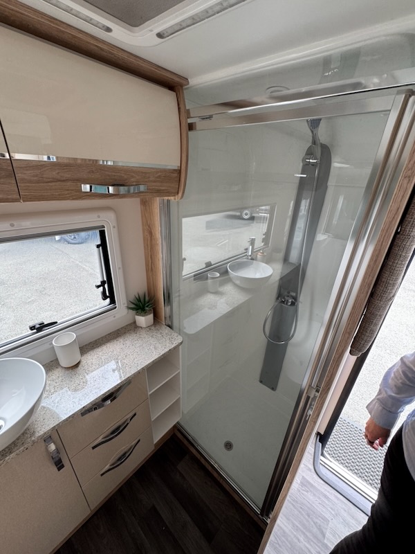 View inside the ensuite facing the back right. A shower cubicle with glass door can be seen, as well as some cabintary on the back wall. There's also a window looking out the back.